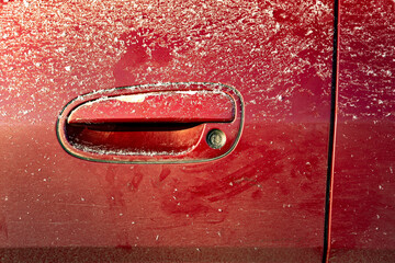 Close-up of a car door handle on an early winter morning, lightly dusted with snow after driving on a winter city road.