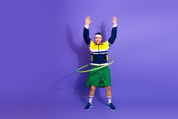 Energetic young male athlete practicing with a hula hoop, wearing retro style sportswear, on a...