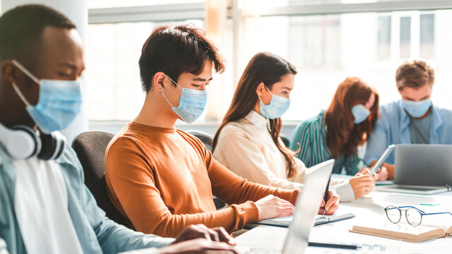 Teamwork in corporate company and returning to work after quarantine covid-19. Focused millennial people wearing medical masks working using laptop and tablet, writing at workplace in office interior - Powered by Adobe