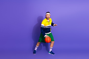 Obraz premium Retro styled male athlete playing basketball in active sportswear on a vibrant purple background, exercising in action