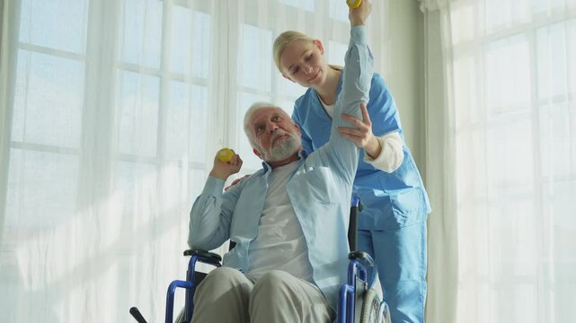 Support rehabilitation healthcare. Nurse helps old man patient in wheelchair picking up dumbbells. Paralyzed man in chair for people with disability doing sports exercise with nurse. Medical caregiver