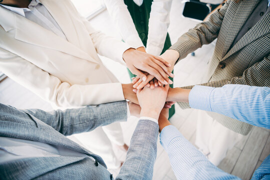 Professional team members placing hands together during a collaboration showing teamwork, unity, and motivation in the workplace