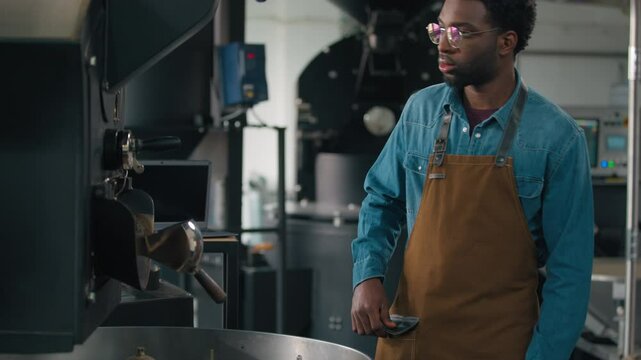African American man working approach roasting machine pull lever coffee beans falling out roasted cocoa male roaster in apron guy at modern factory professional barista technician preparing caffeine