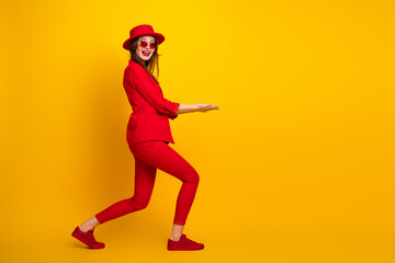 Young woman in vibrant red suit presenting an imaginary object against a bold yellow background while gesturing stylishly