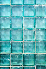 Transparent turquoise glass bricks with weathered surface texture showing interconnected cracks forming a chaotic pattern, vertical