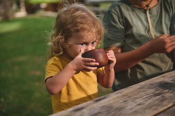 Young Child Drinking Outdoors With Family at a Rustic Table