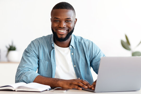 Fototapeta Portrait Of Smiling Successful African American Male Entrepreneur Posing At Workplace In Modern Office, Handsome Black Man Sitting At Desk With Laptop Computer And Looking At Camera, Copy Space