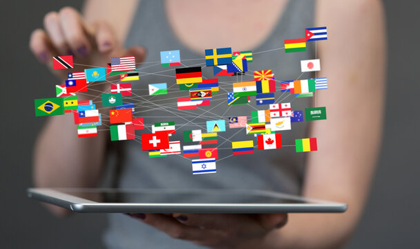 Image of hands holding a tablet displaying a network of interconnected world flags, symbolizing global communication and connectivity.