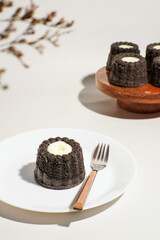 Mini black glutinous rice cake with cheese filling served on a white plate and fork, with others displayed on a wooden cake stand.