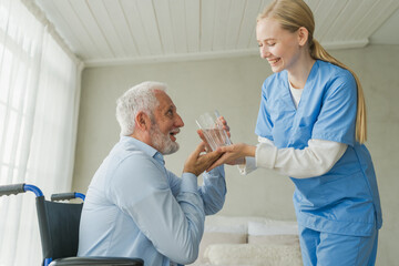 Help support healthcare water balance. Nurse giving glass water for old man patient in wheelchair. Paralyzed man in chair for people with disability drinking fresh water. Senior man and nurse at home