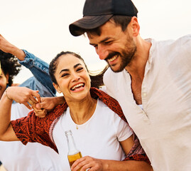 Group of young cheerful people, happy couple in front,  having fun walking and drinking beer at the party on the beach looking happy, Enjoying youth and freedom concept, love and bonding