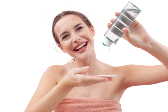 Smiling young woman pouring micellar water onto a cotton pad before cleansing her face. Skincare routine, makeup removal, healthy skin. Isolated on white background, beauty and hygiene concept.