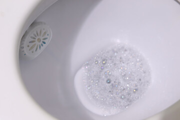 A toilet rim block creating foam in the water, set against a clean white background, symbolizing hygiene and freshness. Fresh and clean toilet rim