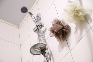 A silver shower head and a white washcloth on clean tiles in a modern bathroom, ready for a refreshing shower. Spotless white tiles frame a silver shower head and a fresh washcloth