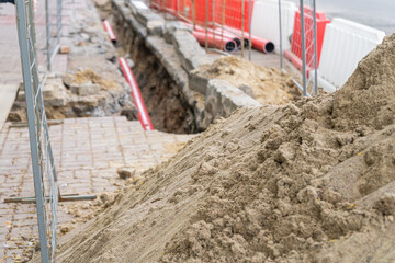 Road repairs, pipe, pile of sand. Red and white plastic barriers blocking the road.