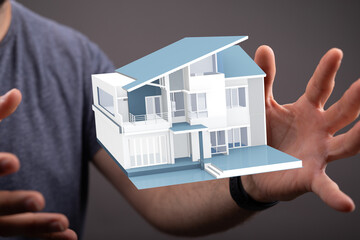 A person's hands gently hold a 3D model of a modern house, perfect for real estate, architecture,...