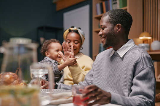 Happy African American man enjoying time with family sharing festive dinner with child and wife at dining table full of delicious food at home