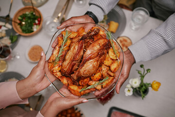 Top view of female hands holding large plate of roasted chicken and vegetables passing dish during...