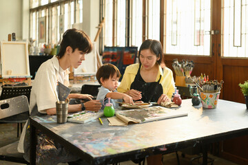 Little child enjoying painting with brush and palette in a hands-on learning art session. Family and teacher support enrich the creative experience