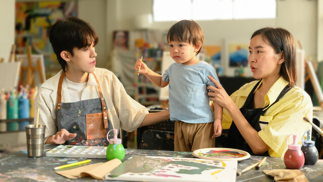 A young child holds a paintbrush while mom supports and guides during an art class session. Creative family bonding in a studio, Family Art Workshop Concept