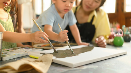 Close-up of preschool children painting on canvas during an art class, guided by a caring teacher in a creative learning environment