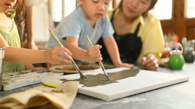 Close-up of preschool children painting on canvas during an art class, guided by a caring teacher in a creative learning environment