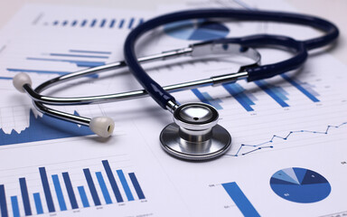 A professional stethoscope resting on a collection of medical charts with blue and white graphs analyzing data