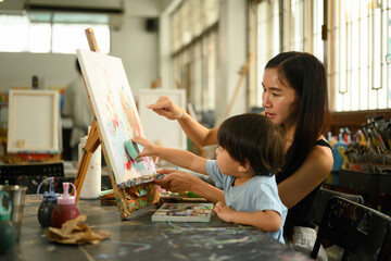 Parent and child sharing creative time together with paint, brushes, and an easel in a cozy classroom