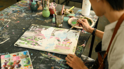 A close-up view of a young person painting abstract patterns with pastel colors on canvas in a creative art studio