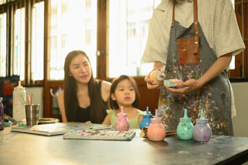 A focused shot of a teacher demonstrates sponge painting technique to a parent and child, hands-on...