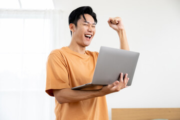 Asian Excited young man celebrating success holding laptop