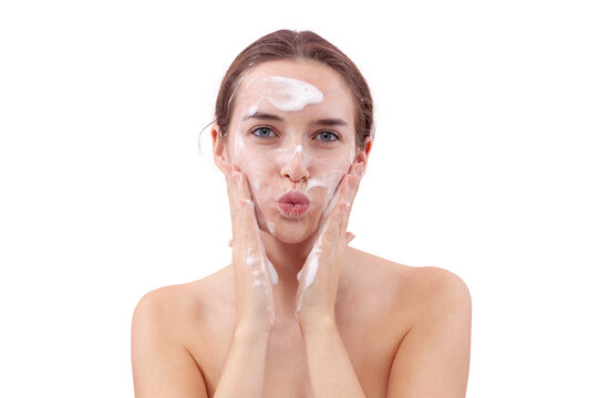 Young woman washing her face with foaming cleanser, hands covered in foam touching her skin. She blows a kiss toward the camera. Skincare routine for clean, healthy face. Isolated on white background - Powered by Adobe