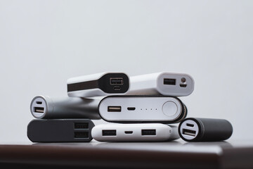 Stack portable power bank chargers of different shapes and sizes on a wooden table. Energy concept,...