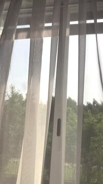 Curtains on the window are blown by the wind. The view from the room to the outside through the windows.