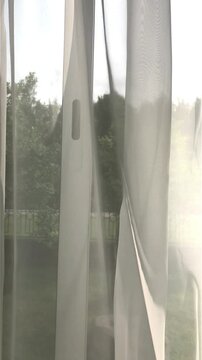 Curtains on the window are blown by the wind. The view from the room to the outside through the windows.