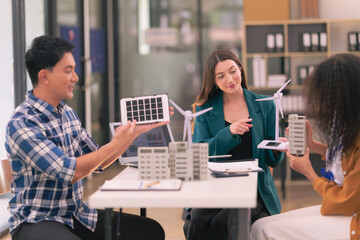 Team of engineers meeting with wind turbines with house models and blueprints placed on tables with solar panels to design renewable energy using wind and solar power.