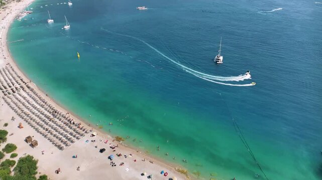Turquoise water, white sand beach, green trees and mountains surrounding the famous oludeniz blue lagoon in fethiye, turkey, with tourists enjoying water sports