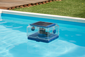 Solar powered pool cleaner floating in a blue swimming pool with green grass in the background