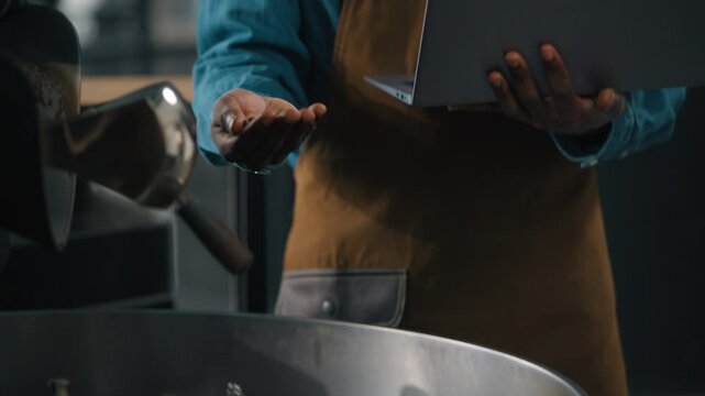 African American man working in roasted coffee fabric inspecting caffeine beans quality holding in hand typing laptop engineer technologist checking roasting machine male roaster guy industry check