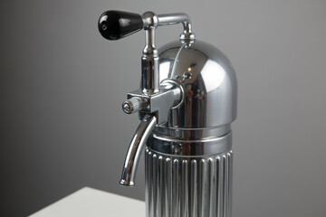 Close up view of a vintage chrome seltzer bottle with a black handle and a gray background behind it