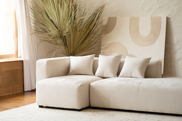 A spacious living area showcases a contemporary sectional sofa adorned with cushions, complemented by a large dried palm plant in a bright and airy setting.