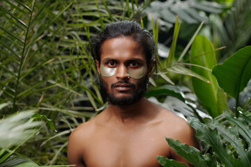 Portrait of young man with eye patches looking straight at camera in lush tropical environment surrounded by green foliage