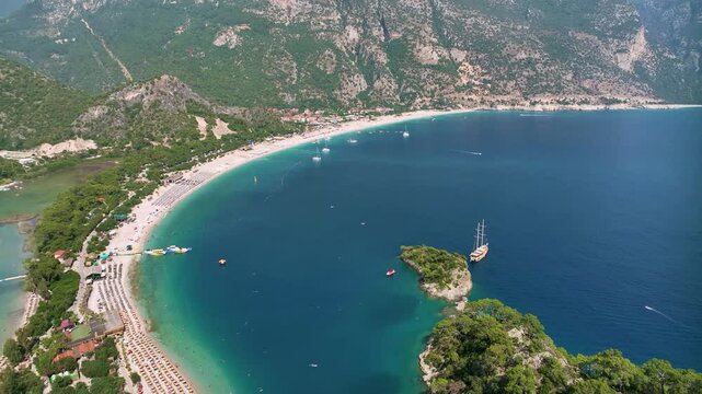 Turquoise water gently laps the shore of oludeniz blue lagoon, a stunning natural wonder nestled between lush green mountains, where a majestic gulet rests near a small, verdant islet