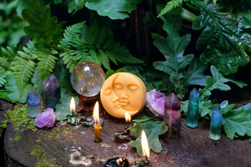 moon amulet, magic crystal ball, minerals and candles on tree stump in forest, natural background. wiccan witch altar. spiritual practice for meditation, relax. esoteric ritual with gemstones.