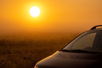 A fascinating panorama of a field unfolding under the morning sky at sunrise. A car is parked on an autumn meadow, bathed in the first rays of light.
