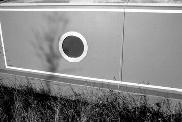Grainy analog monochrome 35mm photo of wall with circular window and shadow of tree