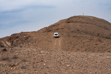 White SUV driving on a rugged dirt road through a barren mountain landscape