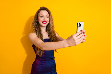 Young fashionable woman taking a selfie with a smartphone against a vibrant yellow background in a...