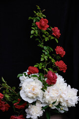 Elegant floral arrangement with lush white peonies and vivid red roses against dark fabric background