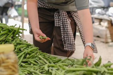 Young woman choosing fresh organic vegetables at a local market. Concept of eco lifestyle, sustainable food, mindful consumption, zero waste, farm produce, and conscious living.